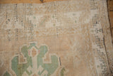 Distressed vintage Turkish carpet corner, beige pile, geometric emerald green motifs, visible wear.