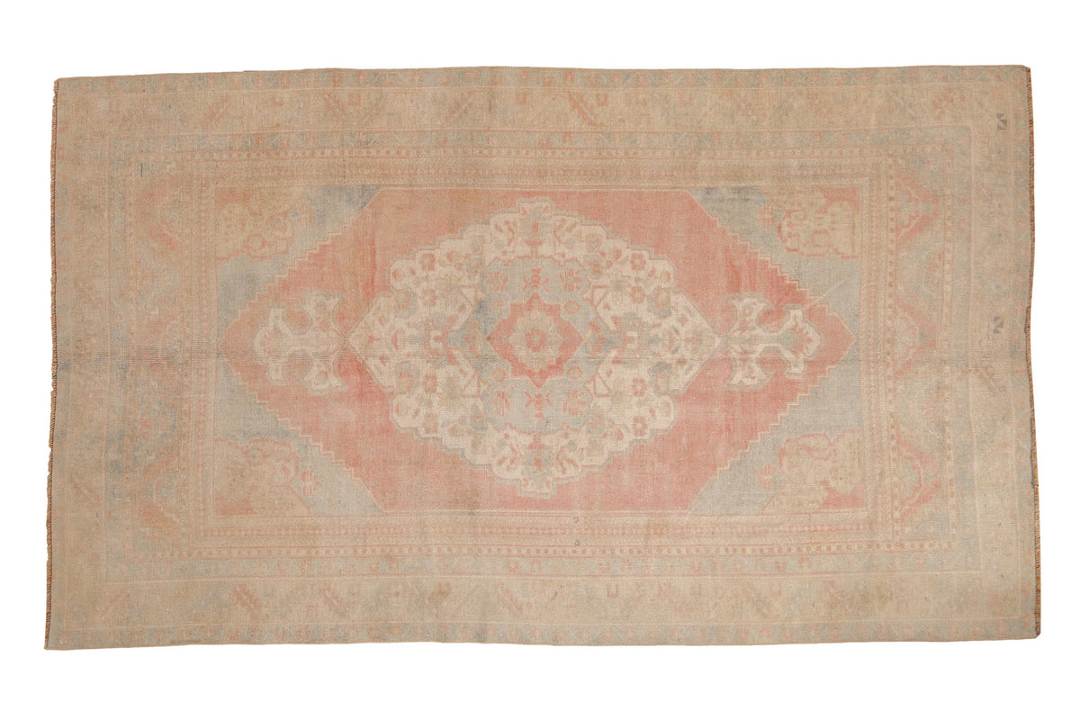 Vintage distressed Oushak carpet with a large scalloped medallion in soft red, pale blue, and beige.