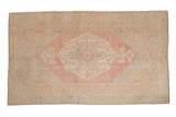 Vintage distressed Oushak carpet with a large scalloped medallion in soft red, pale blue, and beige.