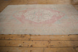A distressed vintage Oushak rug seen from a low angle, showing its low-pile and muted palette.