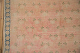 Distressed vintage Sparta carpet close-up, pink field with pale green clover motifs and denim border.