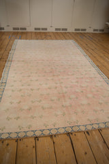 Distressed Sparta carpet with faded blush field, pale green clover leaves, and dusty blue border.