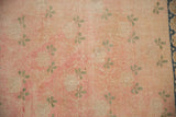 Soft pink distressed field of a vintage Sparta rug with pale green clover motifs.