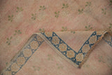 Distressed vintage Sparta carpet: worn pink pile, pale green clovers, and folded blue floral border.