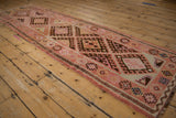 Kurd runner's serrated floral leaves and checkered border in blush and brown.