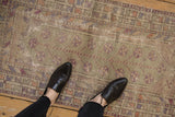 Feet on a distressed vintage Oushak runner, showcasing time-softened aubergine and terracotta blossoms.
