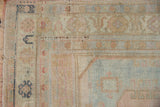 Corner detail of a distressed Oushak showing the stylized pomegranate border in soft pastel tones.