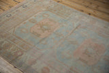 Angled view of a vintage Oushak rug showing its soft, faded texture and pastel-toned gul medallion.