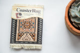 Navajo CoasterRug in packaging, displaying Southwestern geometric patterns, browns, black, and white fringe.