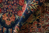Rolled edge of vintage Qazvin rug highlights indigo pile and red floral vine border.