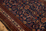 Vintage Malayer rug corner, showing tattered edge and intricate ruby red, beige, and blue borders.