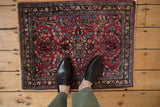 A vintage Sarouk rug mat with cherry red and navy floral bouquets shown for scale.
