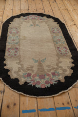 Angled view of the oval vintage Fette-Li rug showing its floral basket and scalloped charcoal border.