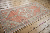 Distressed Oushak rug corner highlights faded orange, pale green, and aubergine colors.