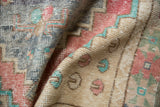 Distressed Oushak rug showing blush, turquoise pac-man floral motifs, and low pile wear.