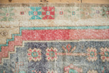 Vintage distressed Oushak rug pile showing worn texture and pale red, blue, sand patterns.