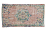 Distressed vintage Oushak rug, dusty rose field, faded teal medallion, and vine border, 2'4