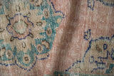 Distressed Oushak rug close-up reveals worn knot heads, dusty rose, faded turquoise, and cream tones.