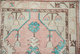 A vintage Oushak's worn hand-knotted pile showing turquoise floral and cantaloupe medallion details.
