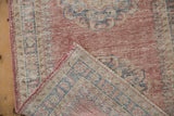 Distressed Oushak rug showing worn blush pile, exposed foundation, and pink side cord.