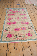 Distressed vintage Oushak rug showing fuchsia blossoms, pale green leaves, and teal accents.