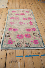 Corner of vintage Oushak rug with fuchsia florals, dusty teal border, fringe, and visible knot heads.