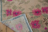 Distressed Oushak rug folded, showcasing fuchsia floral pile, hand-knotted reverse, and original striped selvage.