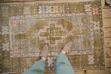 Distressed vintage Oushak rug with low pile texture in olive, gold, and blush.