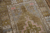 Vintage distressed Oushak rug detail showing faded olive, dusty gold, and pink geometric patterns.
