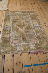 Distressed Oushak rug corner: olive, ivory, dusty rose geometric florals, worn pile.