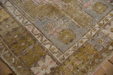 Distressed Oushak rug corner with geometric patterns in olive, gold, grey, and soft pink.