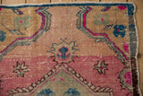 Distressed vintage Oushak runner corner with pink, teal starburst floral motifs.