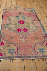 Corner of a distressed Oushak runner with dusty blush, sand spandrels, and fuchsia floral motifs.