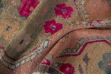 Distressed Oushak rug close-up showing bright fuchsia flowers, subtle teal accents, and abrash texture.