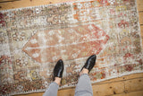 Feet in black shoes on a distressed vintage Oushak rug with faded ivory and red patterns.