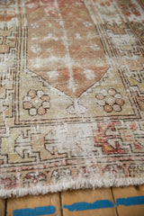 Distressed vintage Oushak rug close-up, showing worn texture, stylized patterns, ivory and apricot tones, fringe.