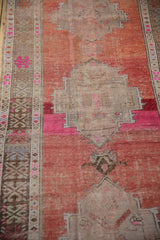 Distressed rust Oushak field with prominent foundation wear, fuchsia band, and geometric border.
