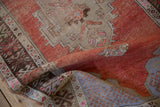 Distressed rust-red Oushak rug pile revealing foundation, alongside folded pale blue patterns.