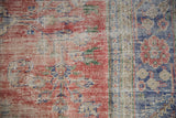 Distressed Turkish Oushak rug close-up with worn red, deep blue pile, foundation visible.