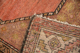Folded vintage Hamadan rug corner, showing worn coral and green pile, with exposed hand-knotted back weave.
