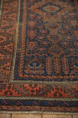 Geometric finned floral blossoms and serrated border in cobalt blue and terracotta on an antique Belouch rug.