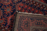 Close-up of Belouch rug corner, showing brick red and navy pattern, fringe, and hand-knotted foundation.