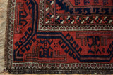 Vintage Belouch rug corner showing brick red field, navy geometric motifs, and goat hair selvage.