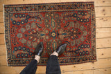 Vintage Sarouk rug's red field, blue quatrefoil blossoms, and floral border, with feet for context.