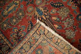 Vintage Sarouk rug corner with cherry red pile, ornate floral border, and tattered ivory fringe.