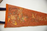 Detail of the worn 'CANADA' text and faded graphic on a vintage orange felt pennant.