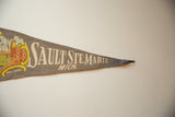 Muted gray felt vintage pennant featuring 'SAULT STE. MARIE MICH.' text and 'SOO LOCKS' graphic.