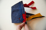 Vintage blue felt pennant close-up, showing fabric tear exposing red, with hand stitching.