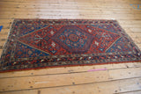 Vintage Hamadan rug's lower corner, brick red field, sapphire blue serrated spandrel, and geometric border.
