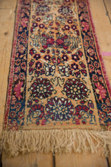 Worn pile of antique Persian Kerman runner, featuring red, navy, apricot floral motifs.